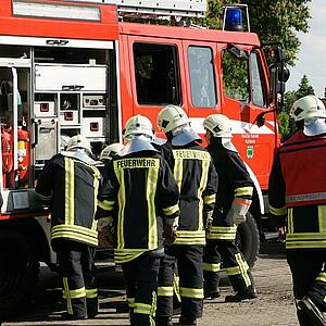 Einsatzkräfte der Feuerwehr stehen an einem Löschwagen.