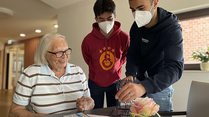 Zwei Jugendliiche beim Bingospielen mit einer Seniorin