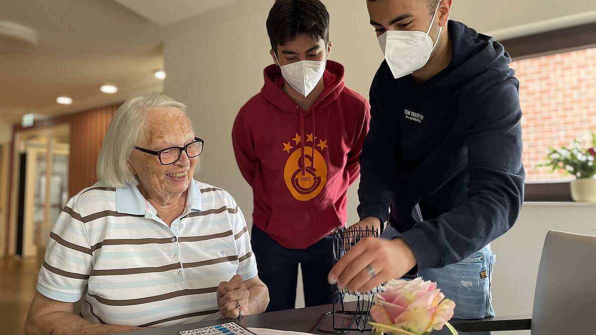 Zwei Jugendliiche beim Bingospielen mit einer Seniorin